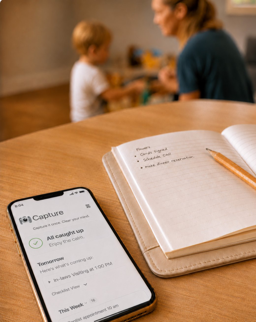 A phone showing a captured list on a kitchen table, a mother and child out of focus behind it